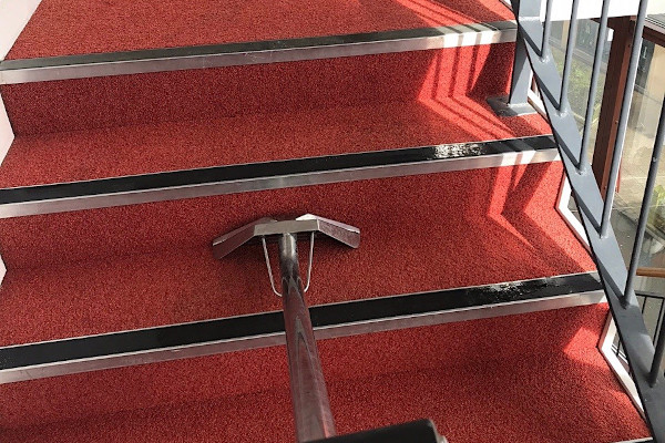 cleaning red carpeted stairs with a carpet cleaning wand