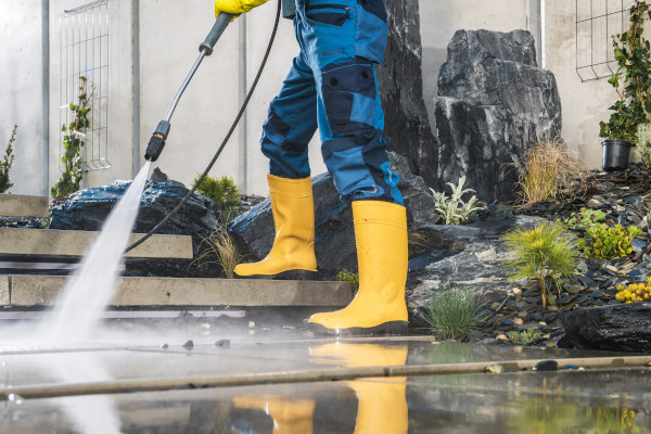 man wearing yellow boots power washing a pathway