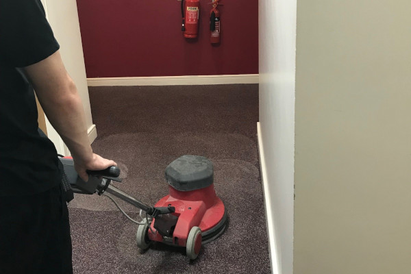 man using a rotary floor cleaning machine in an office corridor