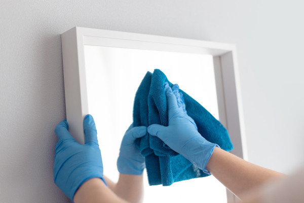 a person with blue gloves cleaning a mirror