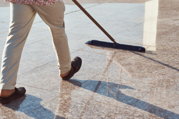 person cleaning an outdoor marble floor with a flat mop