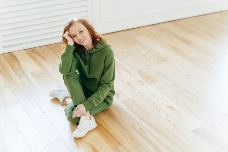 happy women in green outfit sitting on shiny laminate floor