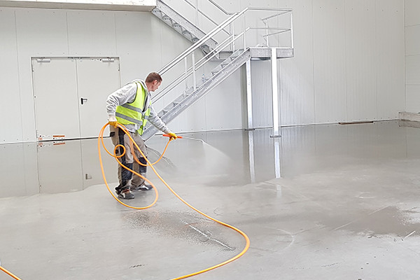 Man in high-vis cleaning floor in empty warehouse